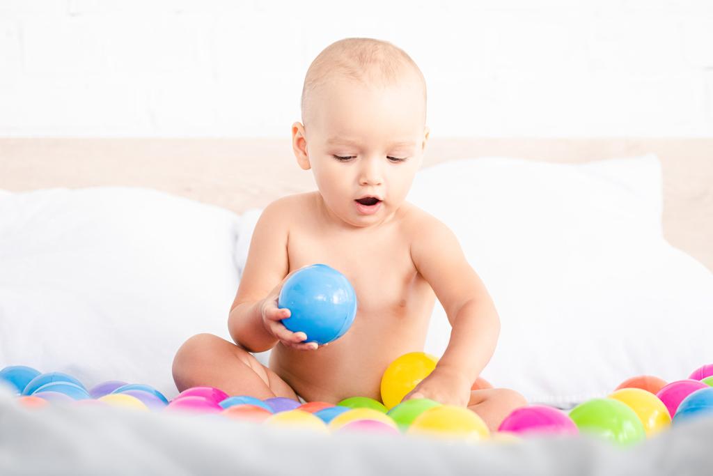 Lindo bebé sentado en la cama y jugando con bolas de colores
 - Foto, Imagen