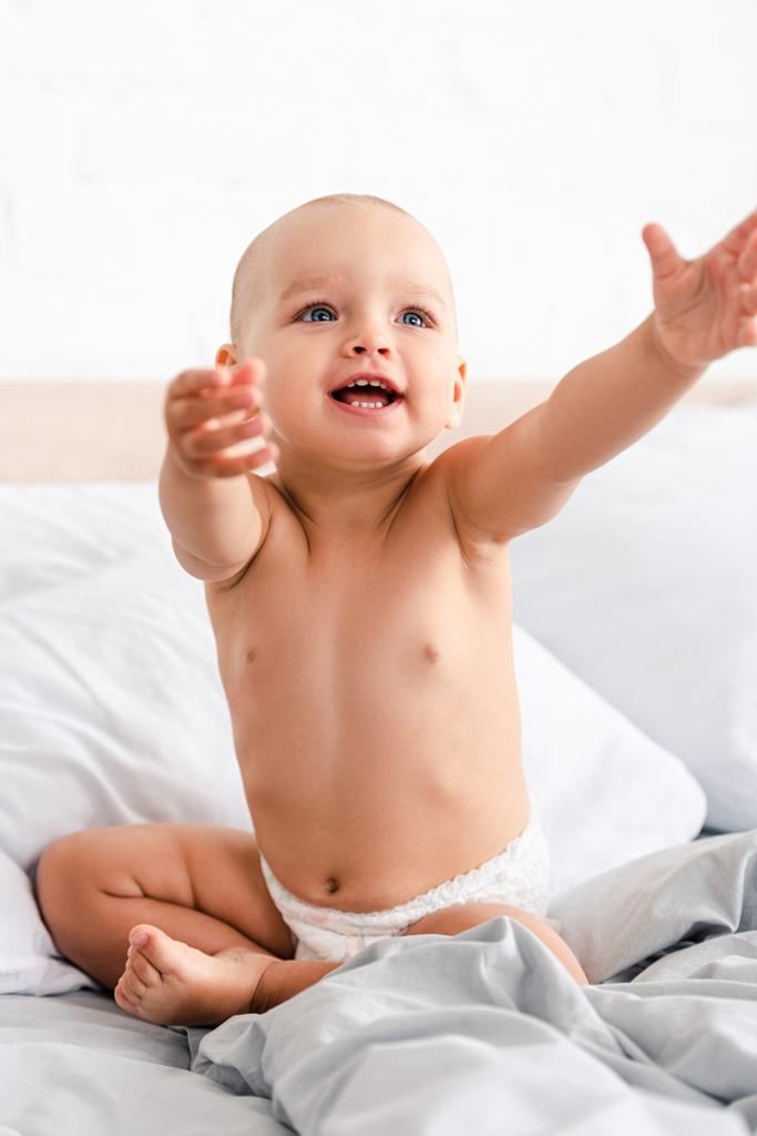 Χαριτωμένο μικρό παιδί σε πάνα χαμογελώντας και σηκώνοντας τα χέρια επάνω - Φωτογραφία, εικόνα