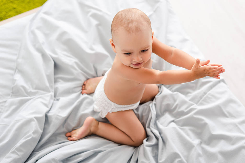 Κορυφαία θέα του μωρού σε πάνα κάθεται στο κρεβάτι και τα χέρια παλαμάκια - Φωτογραφία, εικόνα
