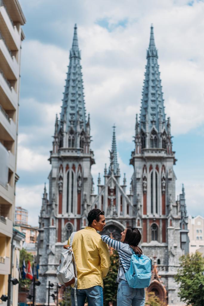 KYIV, UKRAINE - JULY 8, 2019: happy multicultural friends standing near St. Nicholas Roman Catholic Cathedral - Photo, Image
