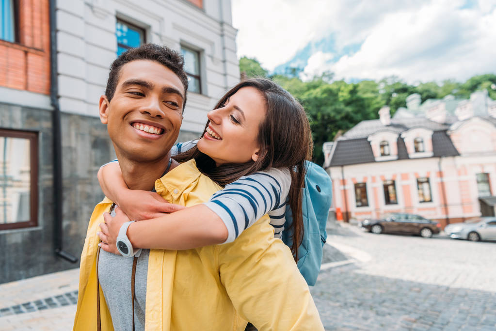 glückliches Mädchen umarmt fröhlich gemischte Rasse Mann in der Nähe von Gebäuden - Foto, Bild