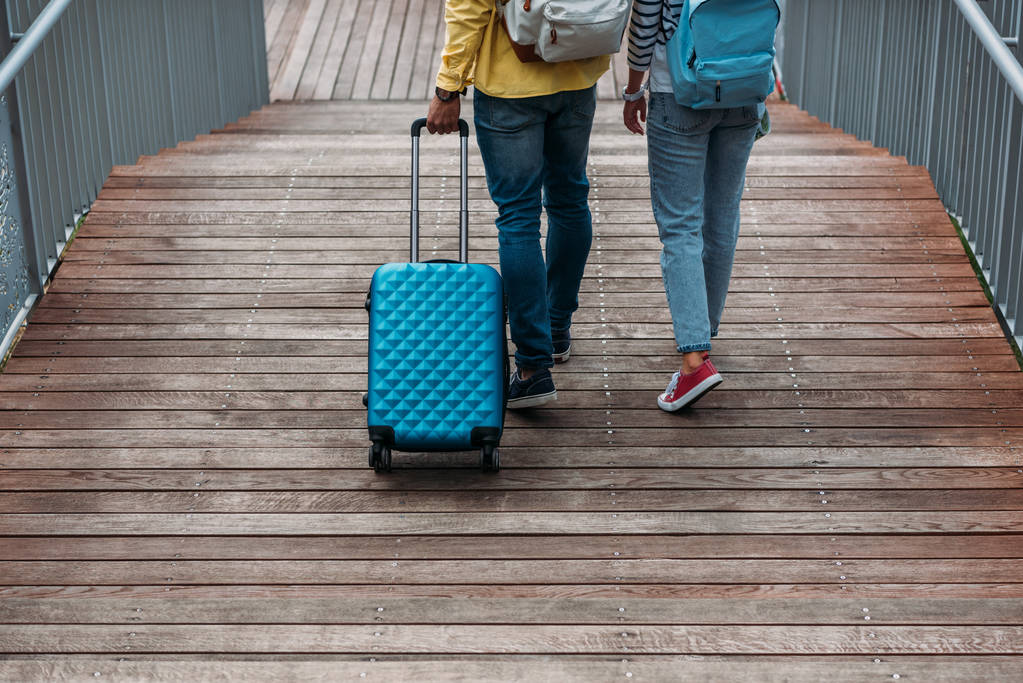cropped view of multicultural man and woman walking with blue luggage  - Photo, Image