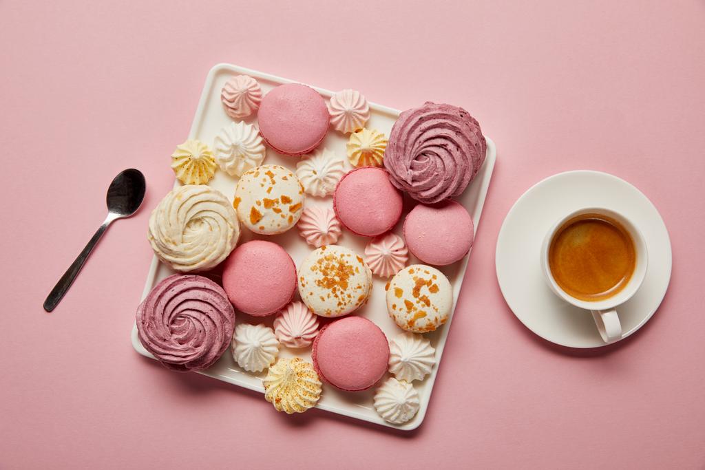 Top view of  meringues and macaroons on square dish with spoon and cup of tea on pink background - Photo, Image
