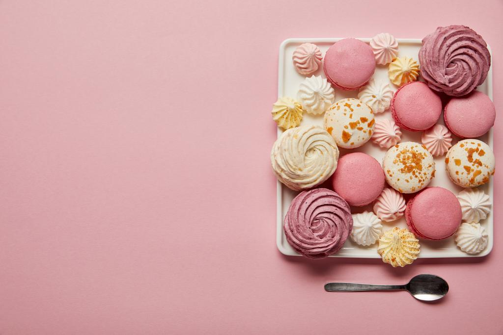 Flat lay with assorted meringues and macaroons on square dish with spoon on pink background - Photo, Image