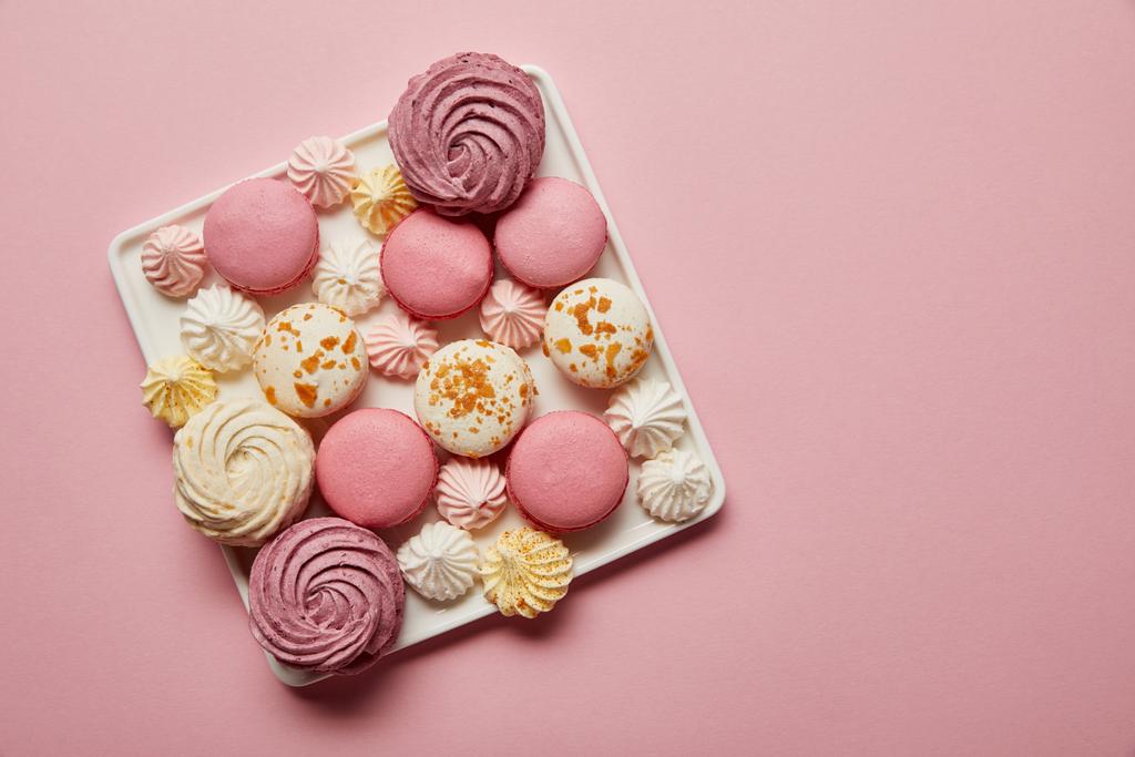 Vista superior de macaroons franceses variados e merengues no prato quadrado no fundo rosa
 - Foto, Imagem