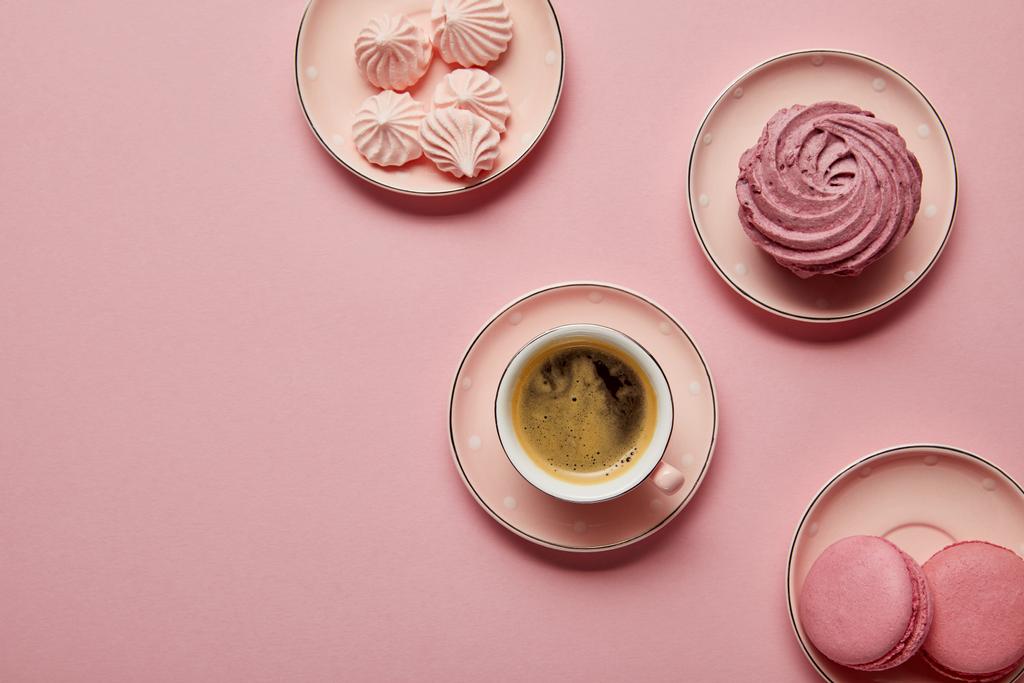 Vista superior de platillos punteados rosados con merengues, macarrones y taza de café sobre fondo rosa
 - Foto, Imagen
