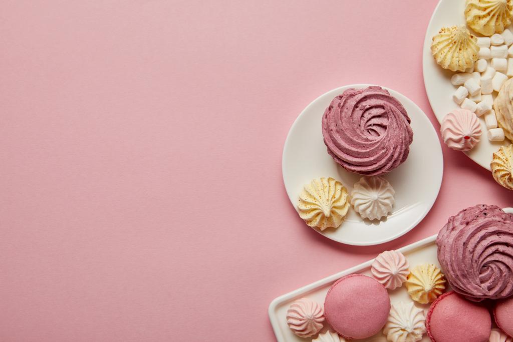 Draufsicht auf rosa, weiße und gelbe Baiser, Makronen und Marshmallows auf rosa Hintergrund - Foto, Bild