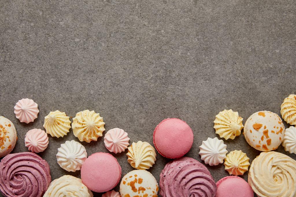 Top view of pink and white macaroons with pink, yellow and white meringues on gray background - Photo, Image
