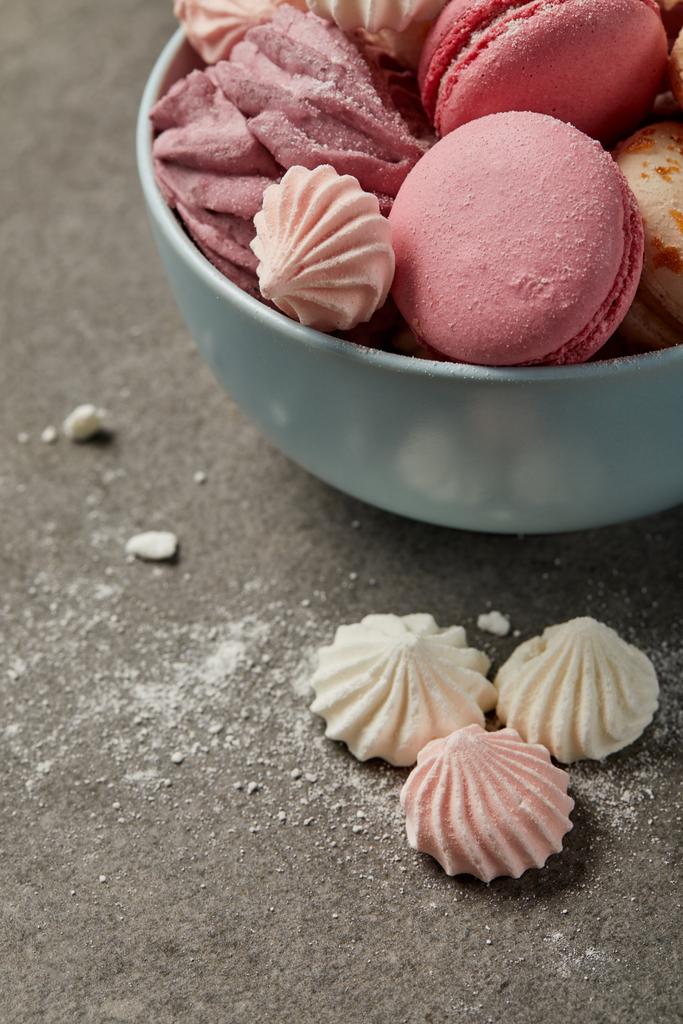 Cuenco azul con deliciosos macarrones franceses, suave zephyr y pequeños merengues rosados y blancos con trozos de azúcar sobre fondo gris
 - Foto, imagen
