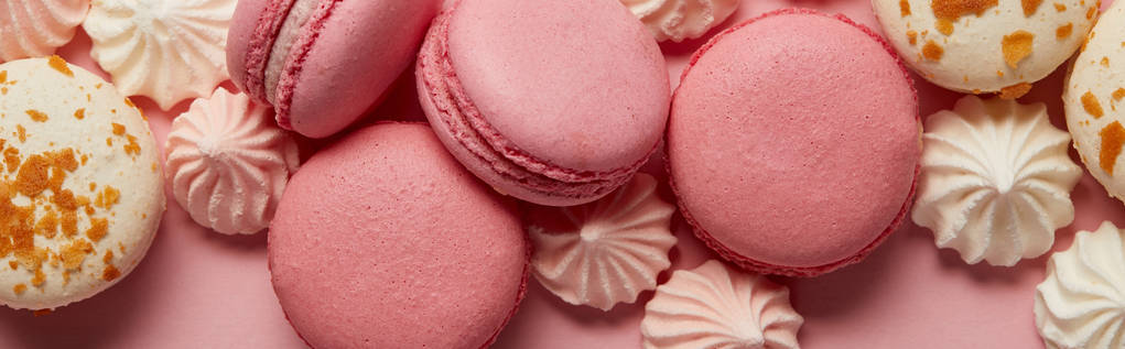 Heerlijk geassorteerde bitterkoekjes met kleine roze en witte meringues op roze achtergrond - Foto, afbeelding