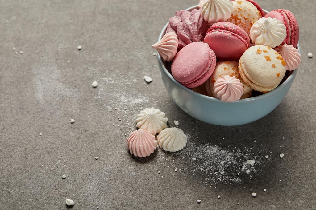 Delicious french macaroons and meringues in blue bowl and smashed sugar pieces on gray background - Photo, Image