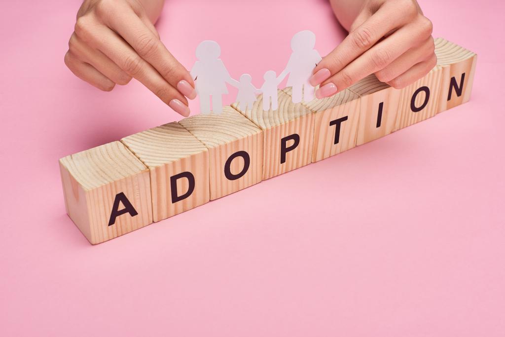 cropped view of woman holding paper cut lesbian family on wooden cubes with adoption lettering on pink background - Photo, Image