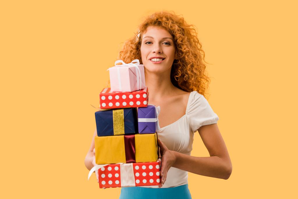 attractive redhead girl holding gift boxes isolated on yellow - Photo, Image