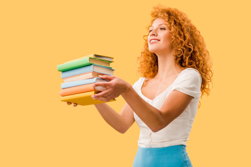 ελκυστική χαμογελαστή μαθήτρια κρατώντας βιβλία απομονωμένα σε κίτρινο  - Φωτογραφία, εικόνα