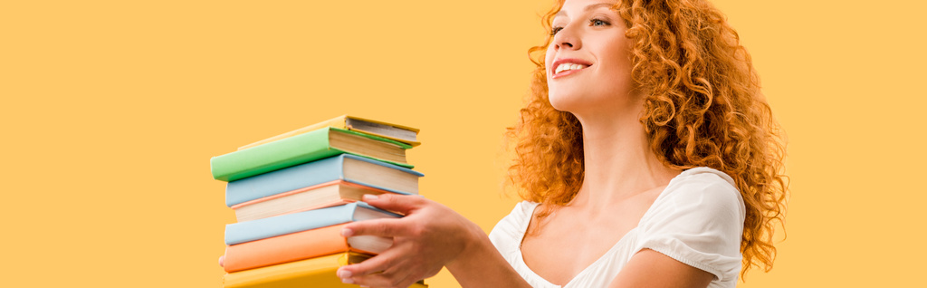 happy redhead student holding books isolated on yellow  - Photo, Image