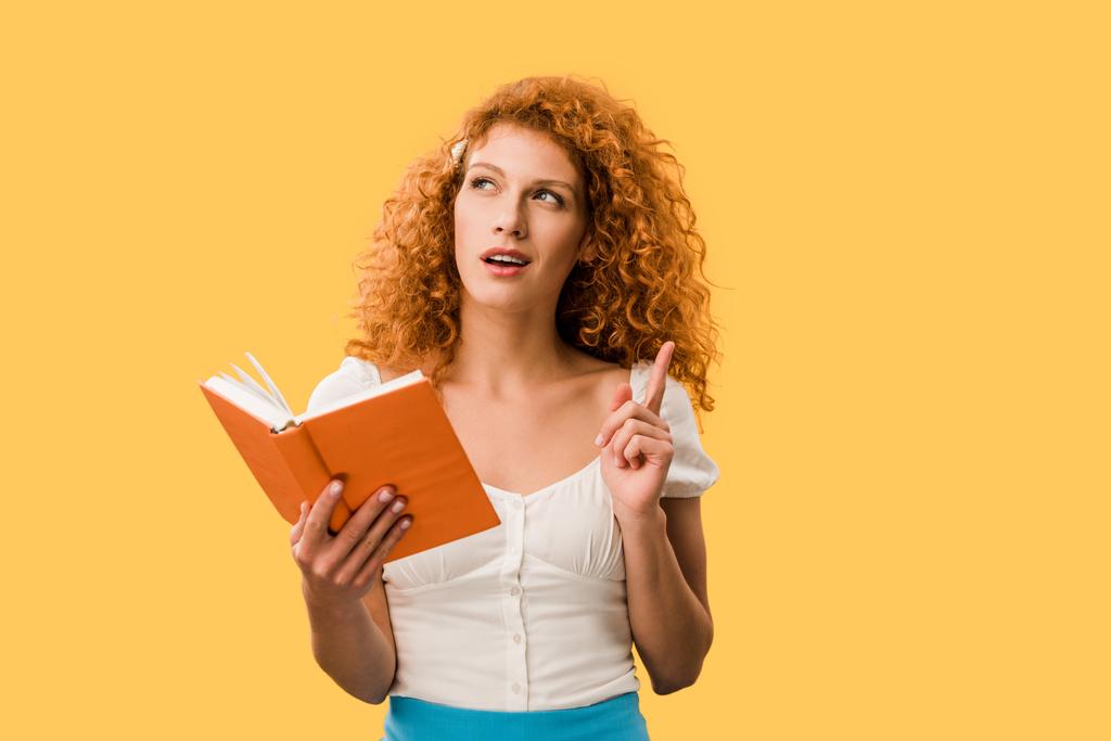 σκεπτική κοκκινομάλλα γυναίκα με το βιβλίο απομονωμένο στο κίτρινο - Φωτογραφία, εικόνα