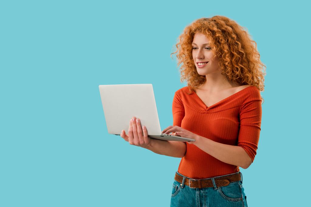 χαμογελαστή κοκκινομάλλα γυναίκα χρησιμοποιώντας φορητό υπολογιστή απομονωθεί στο μπλε - Φωτογραφία, εικόνα
