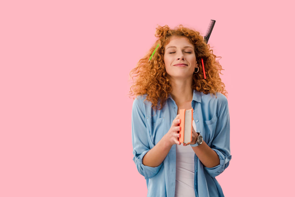 dreamská studentka s tužkami ve vlasech, držící knihu izolovaná na růžovém - Fotografie, Obrázek