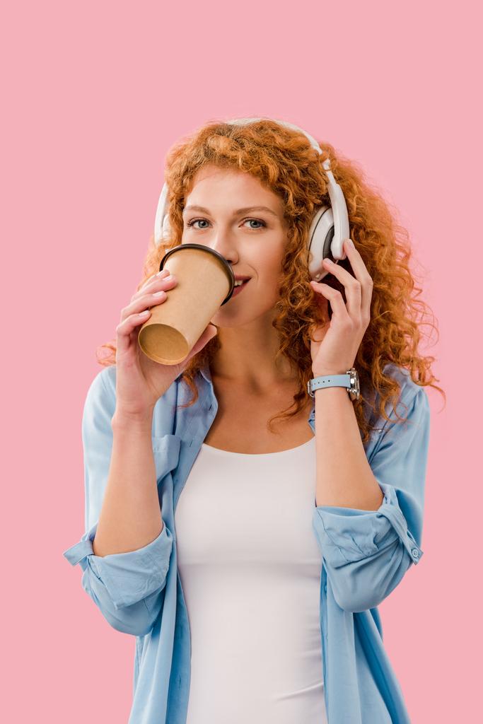 счастливая рыжая девушка, пьющая кофе и слушающая музыку в наушниках, Isolated On pink
 - Фото, изображение