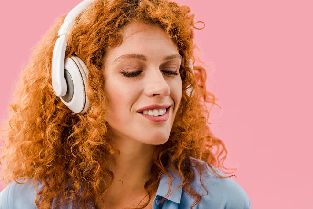 felice rossa ragazza ascoltando musica in cuffia, isolato su rosa
 - Foto, immagini