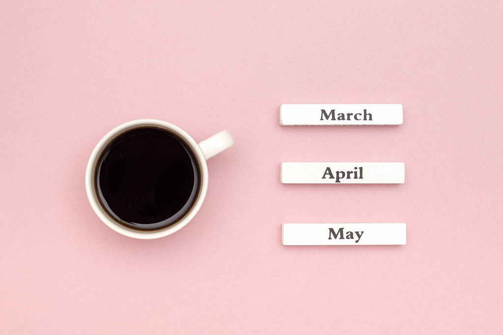 Ξύλινο ημερολόγιο άνοιξη μήνες Μάρτιος, Απρίλιος, Μάιος και φλιτζάνι μαύρου καφέ που κατευθύνεται σε παστέλ ροζ χαρτί φόντο - Φωτογραφία, εικόνα