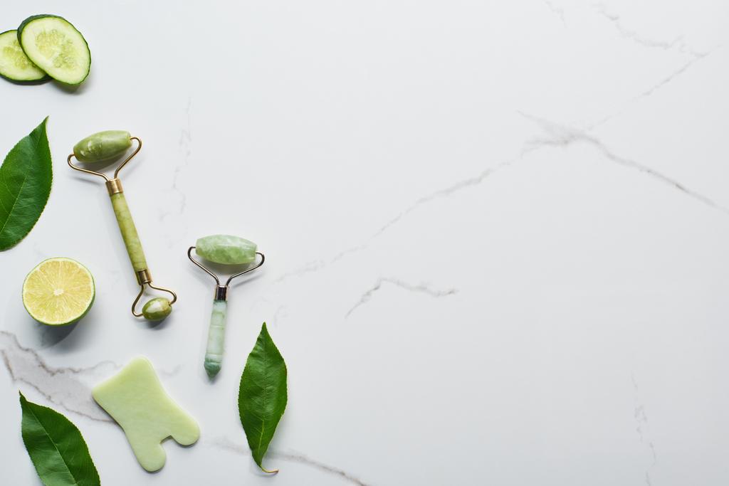 vista superior da espátula, rolos de massagem, folhas verdes frescas, fatias de limão e pepino na superfície de mármore
 - Foto, Imagem