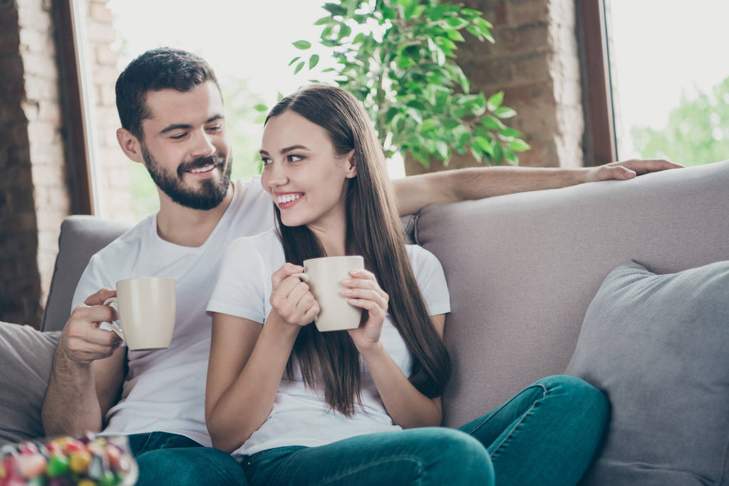 Foto von entzückenden verliebten Paar hält Heißgetränk Hände kommunizieren sitzen gemütliche Sofa drinnen - Foto, Bild