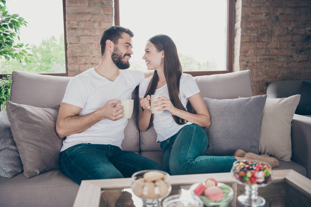 Profile photo of adorable pair in love holding hot beverage hands look eyes sitting cosy sofa indoors - Photo, Image