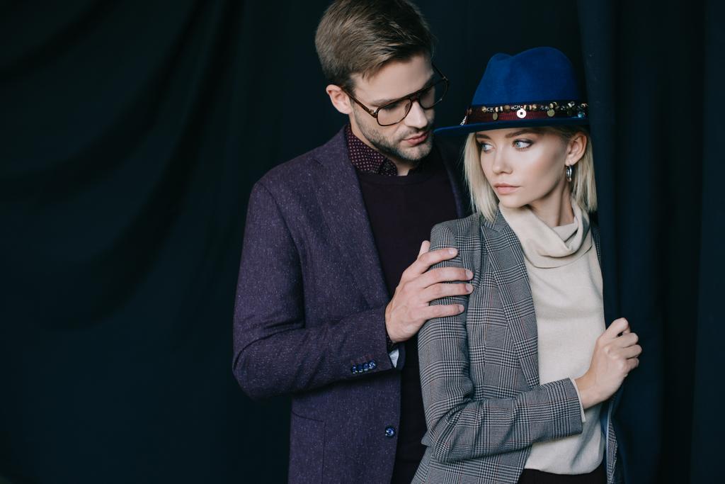 elegant young man in glasses embracing blonde girl in hat near curtain - Photo, Image