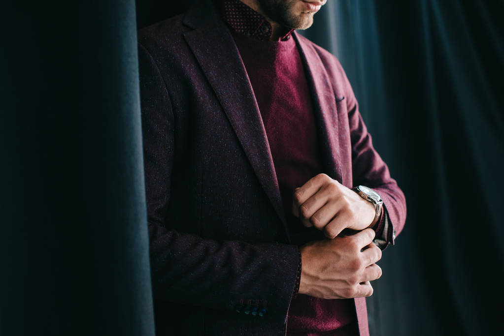 обрезанный вид стильного молодого человека в куртке и наручных часах, стоящих рядом с занавесом
 - Фото, изображение