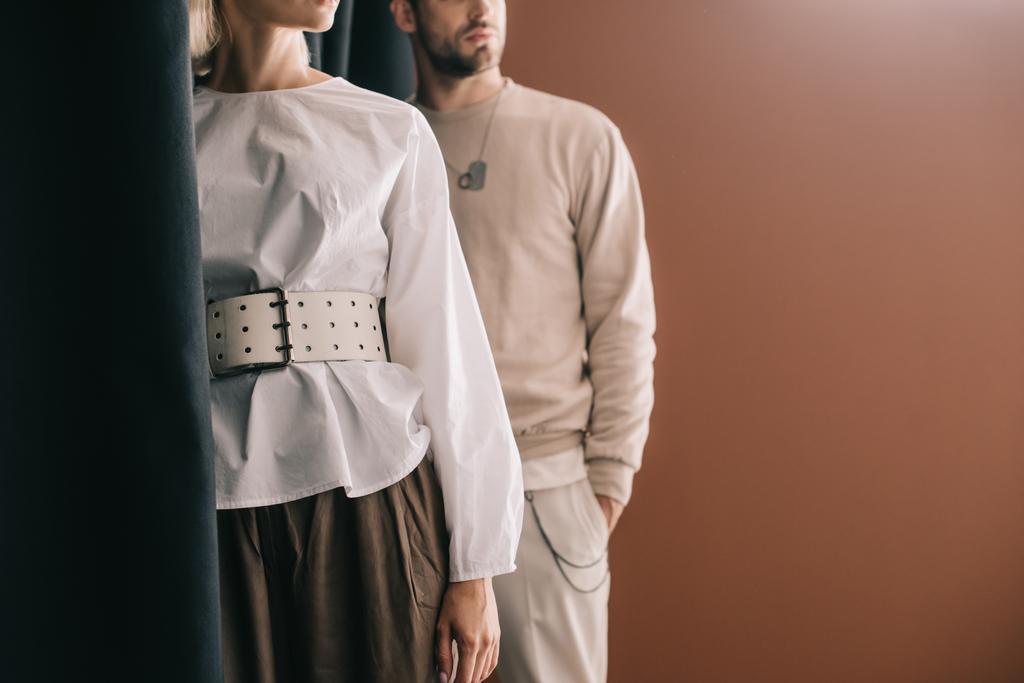 vista cortada de elegante jovem mulher em blusa e homem de pé perto cortina em marrom
 - Foto, Imagem