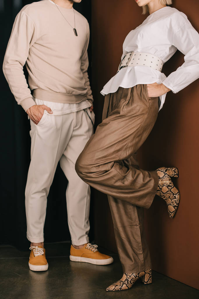 vista recortada de hombre y mujer con estilo en botas con impresión de piel de serpiente de pie con las manos en los bolsillos cerca de la cortina
 - Foto, Imagen