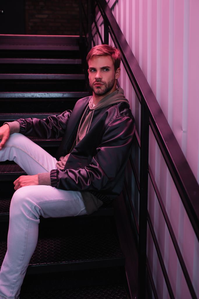 pensive bearded young man in jacket sitting on stairs - Photo, Image