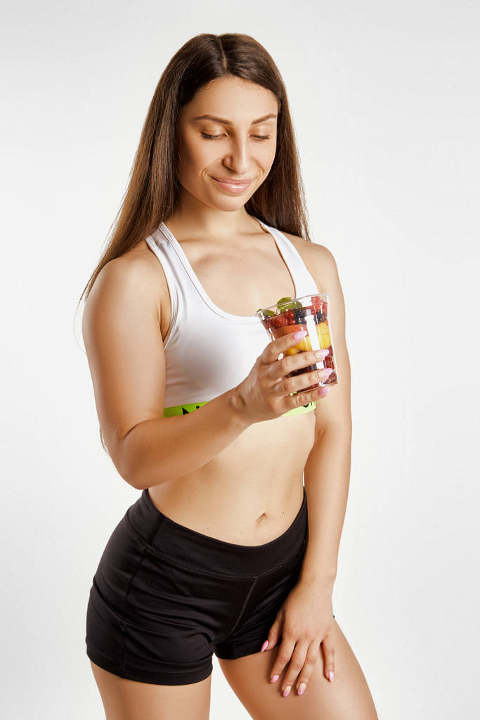 Beautiful muscular girl holding a glass of fruit - Photo, Image