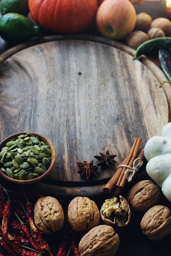 Őszi háttér dekoratív sütőtök, magvak, diófélék, zöldek, gyümölcsök, zöldségek, fűszerek és fából készült tábla hely a szöveg  - Fotó, kép