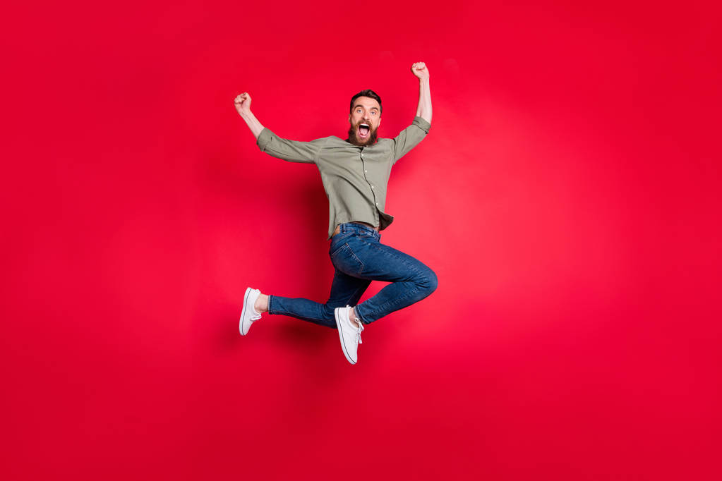Повна довжина тіла фотографія обернутого радісного чоловіка, який стрибає з щастям, бачачи свої командні змагання, ізольовані червоним тлом
 - Фото, зображення