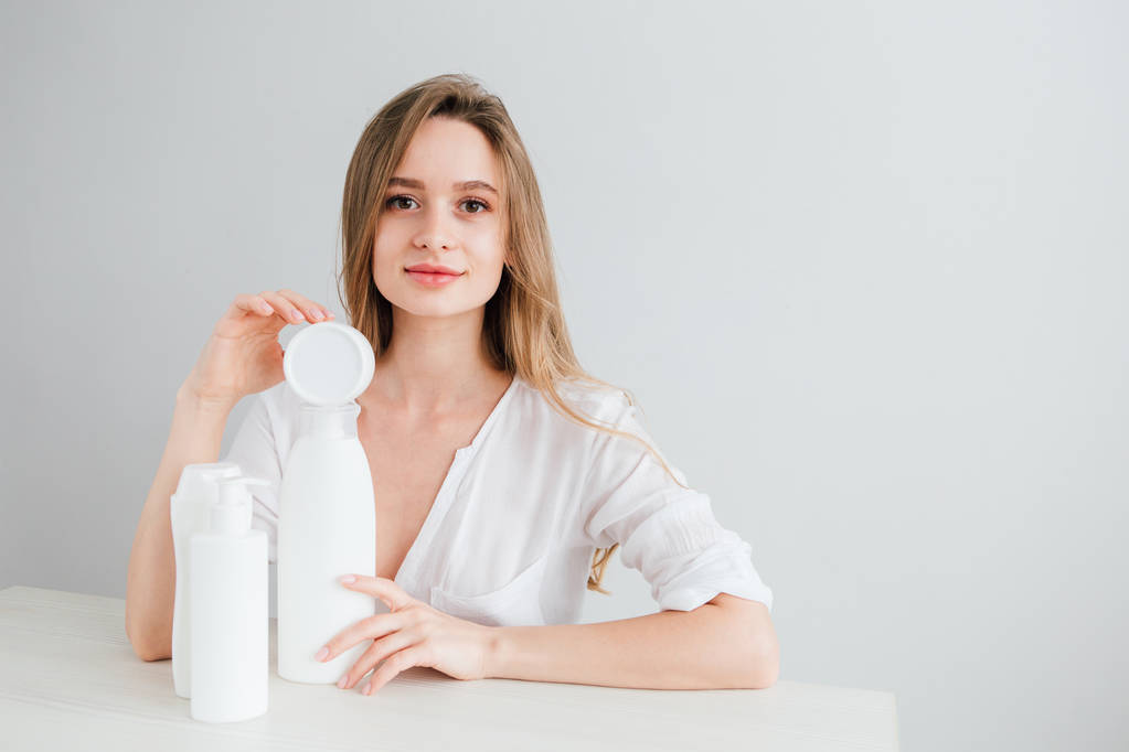 Jong mooi meisje met witte cosmetische flessen van verschillende grootte - Foto, afbeelding