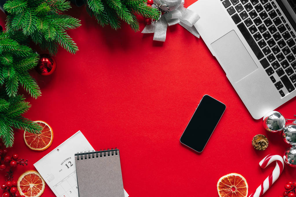 Ordenador portátil con ramas de árbol de piel y decoraciones de Navidad sobre fondo rojo vista superior
 - Foto, Imagen