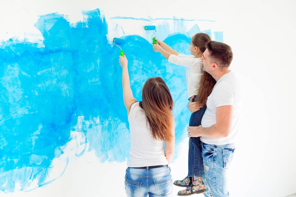 Μητέρα, πατέρας και κόρη βάφουν τον τοίχο στο νέο τους σπίτι.. - Φωτογραφία, εικόνα