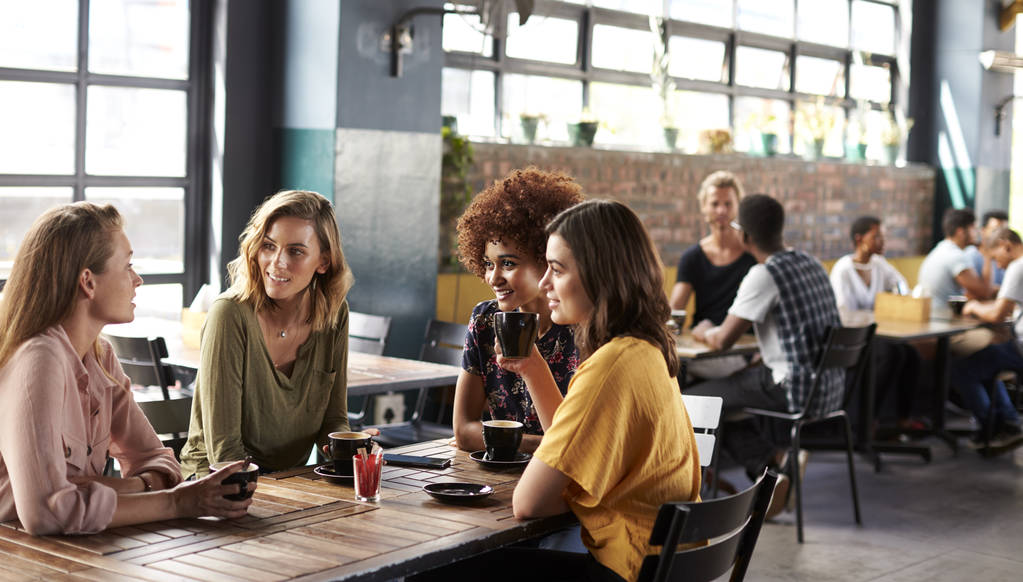 Four Young Female Friends Meeting Sit At Table In Coffee Shop And Talk - Photo, Image