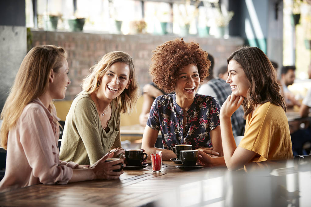vier junge Freundinnen treffen sich an einem Tisch im Café und unterhalten sich - Foto, Bild