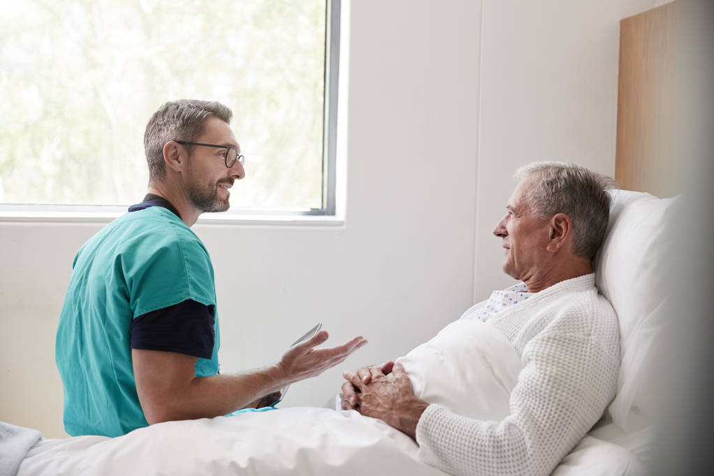 Chirurgo che visita e parla con il paziente anziano maschio nel letto di ospedale nell'unità geriatrica
 - Foto, immagini