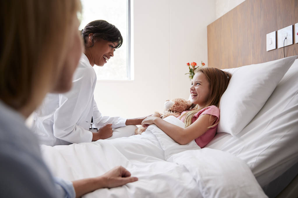 Médico femenino visitando a madre e hija acostadas en la cama en la sala del hospital
 - Foto, Imagen