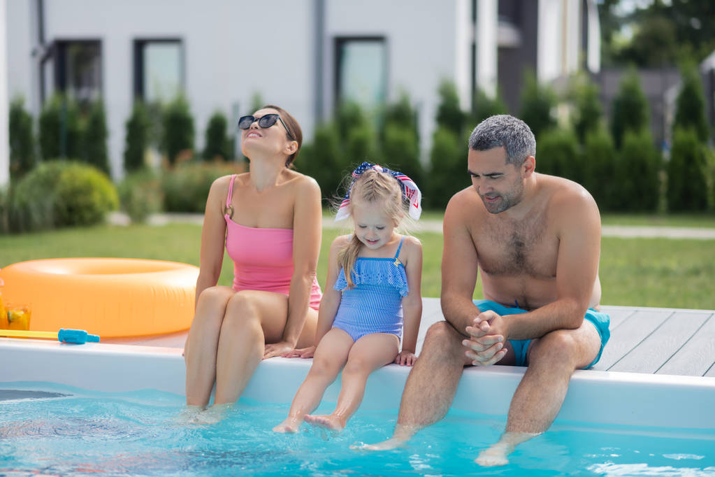 Ebeveynler ve kızı sıcak yaz gününde yüzme havuzu yakınında oturan - Fotoğraf, Görsel