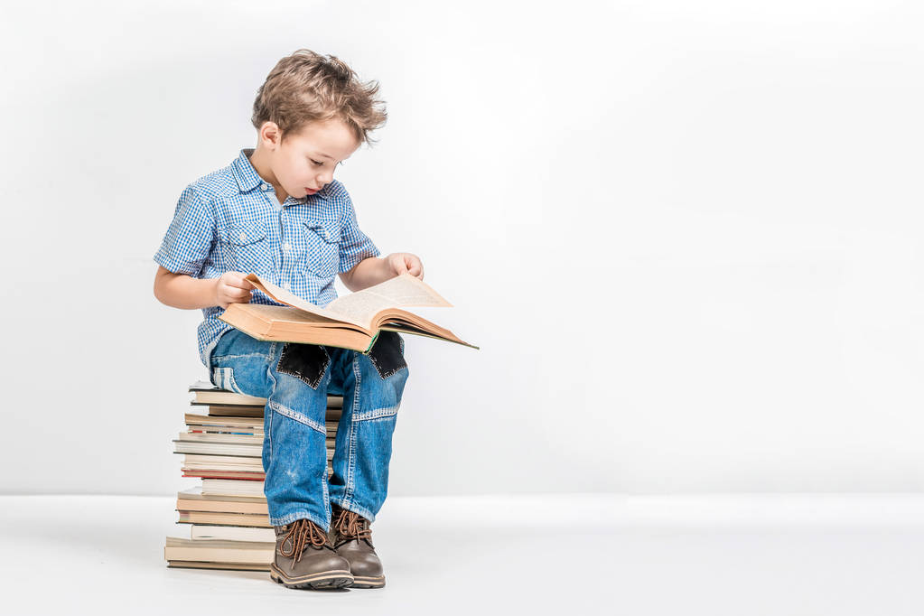 Un chico guapo se sienta en una pila de libros y examina un libro en una w
 - Foto, imagen