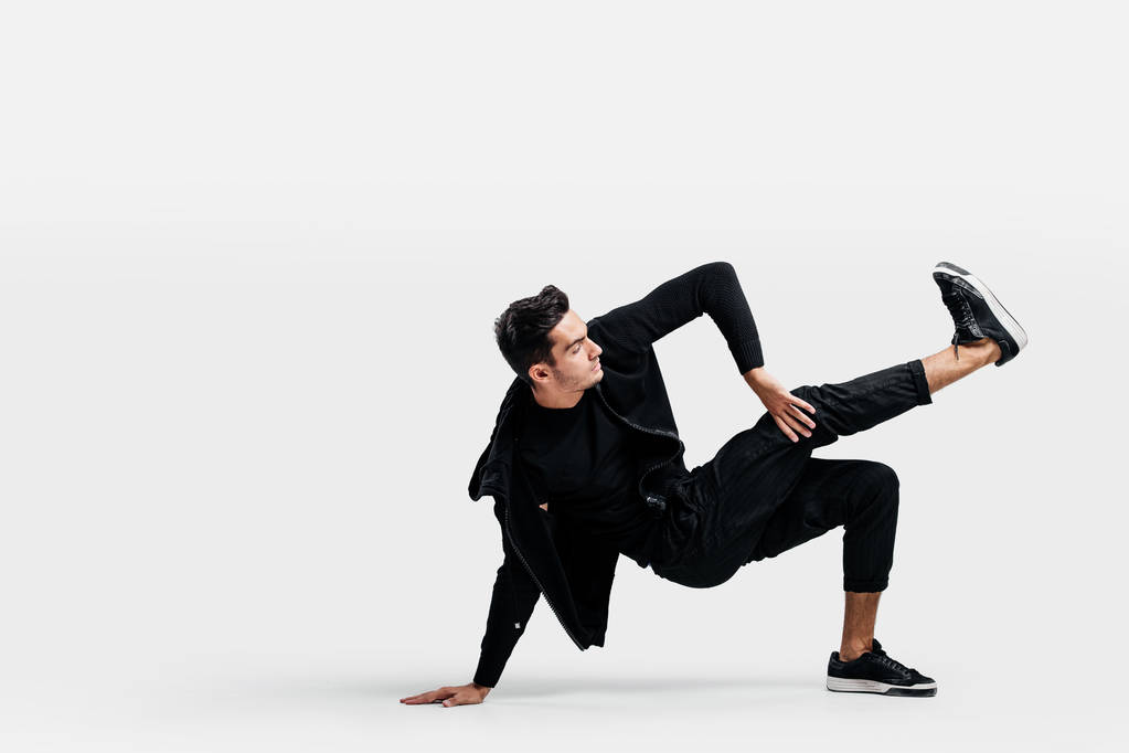 Handsome young man wearing a black sweatshirt and black pants is dancing breakdance doing dancing movements on the floor - Photo, Image