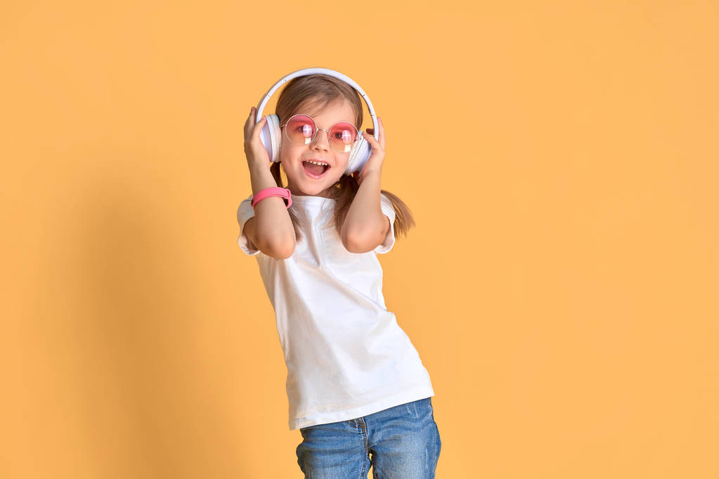 Girl listening to music in headphones on yellow background. Cute child enjoying happy dance music on studio background wall - Photo, Image