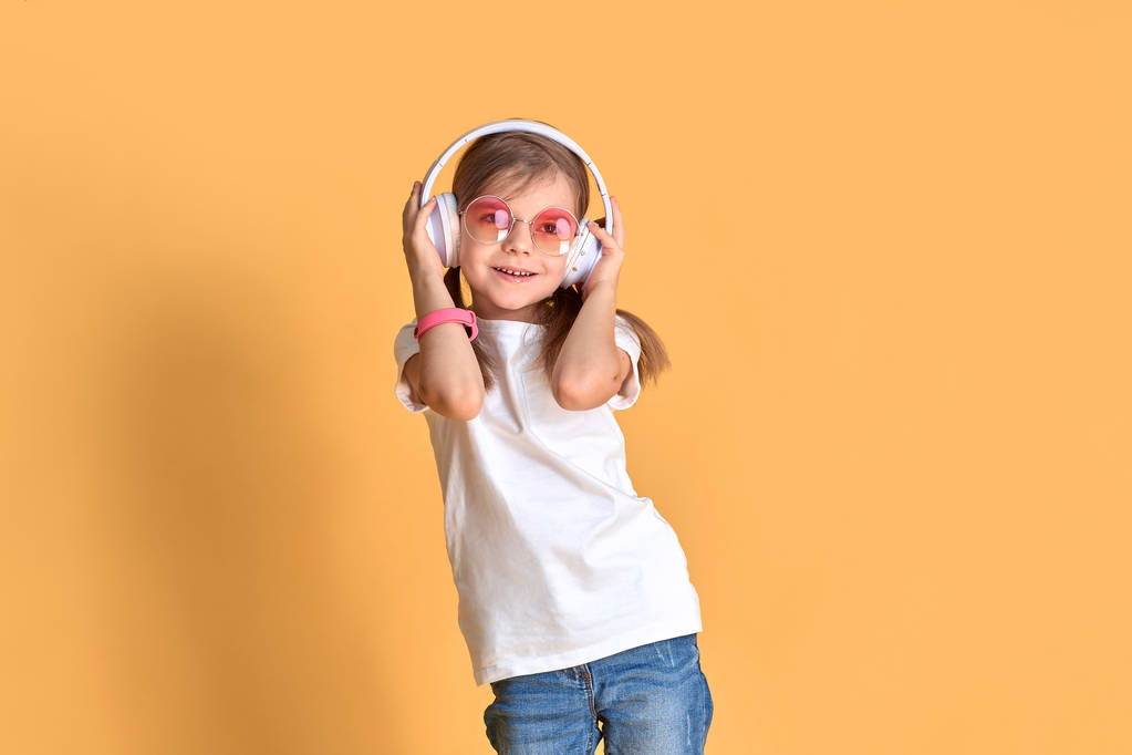 Menina ouvindo música em fones de ouvido no fundo amarelo. Bonito criança desfrutando de música de dança feliz na parede de fundo do estúdio
 - Foto, Imagem