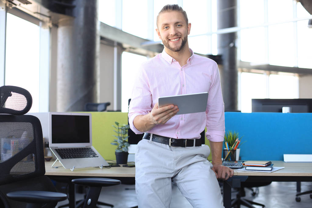 Νέος σύγχρονος επιχειρηματίας που εργάζεται χρησιμοποιώντας ψηφιακό δισκίο ενώ κάθεται στο γραφείο. - Φωτογραφία, εικόνα