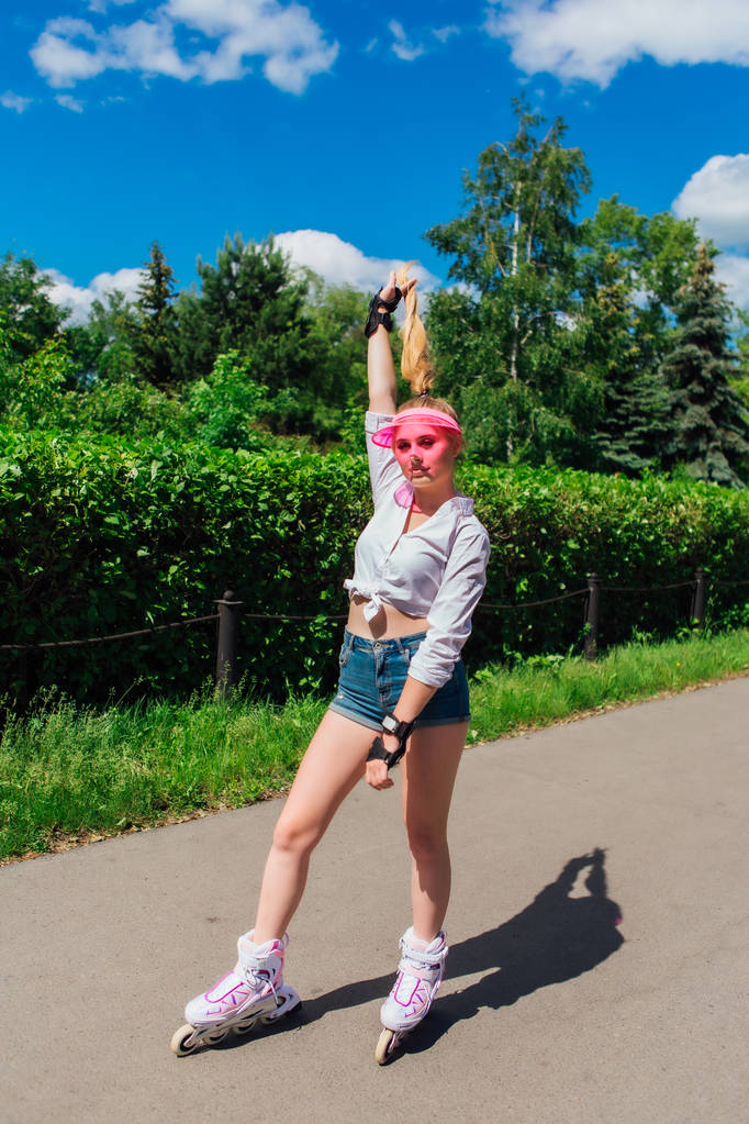 Porträt eines emotionalen Mädchens mit rosafarbenem Schirm und Schutzhandschuhen für Rollerblades und Skateboarden auf Rollerblades unterwegs. - Foto, Bild